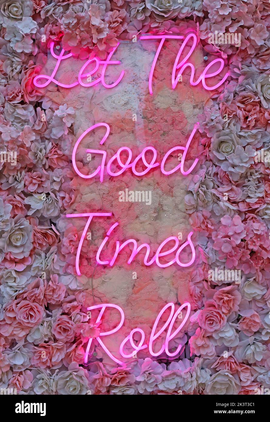 Lass die guten Zeiten Rollen, rosa Neonschild auf Blumen - optimistisch Stockfoto