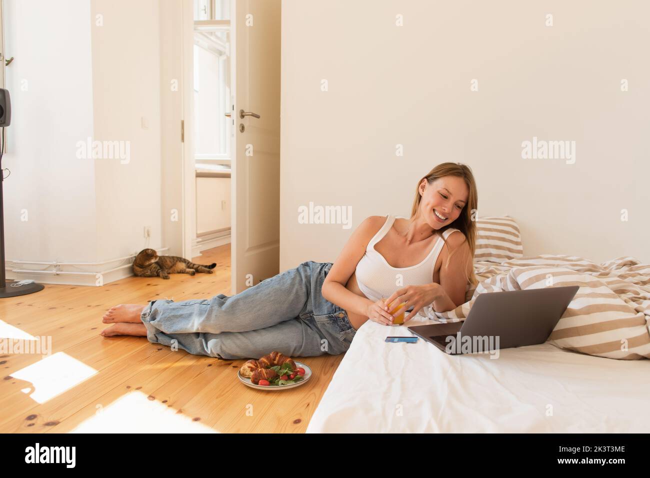 Junge Frau mit Orangensaft in der Nähe des Laptops und Frühstück im Schlafzimmer, Stockbild Stockfoto