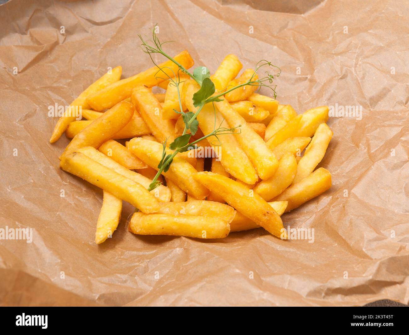 Leckere pommes frites, die mit mikrogrünen Erbsen auf Bastelpapier verziert sind Stockfoto