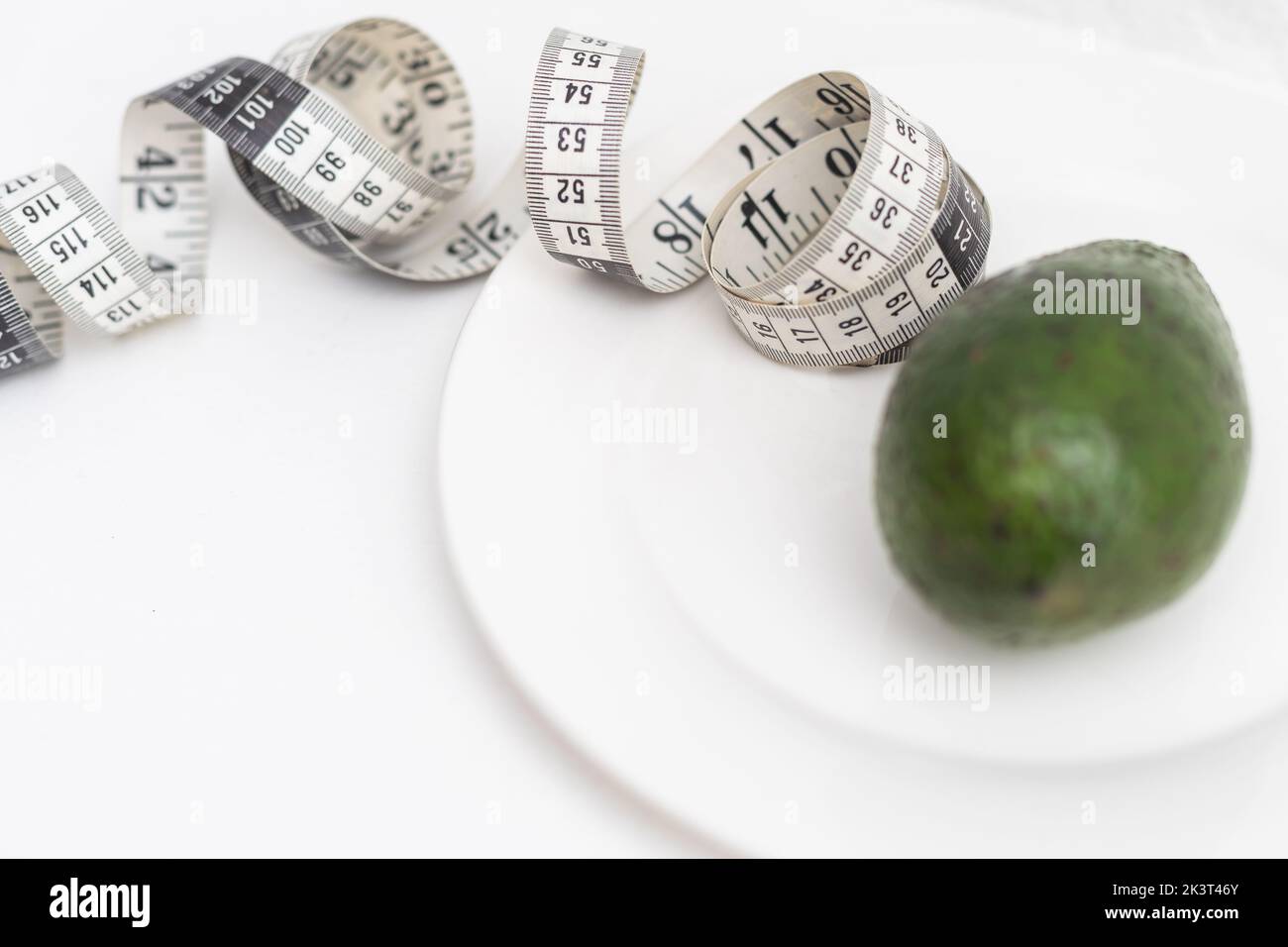 Kreative flache Lay-Komposition aus einer ganzen grünen Avocado und weichem Maßband auf einer weißen Platte isoliert auf Weiß. Stockfoto