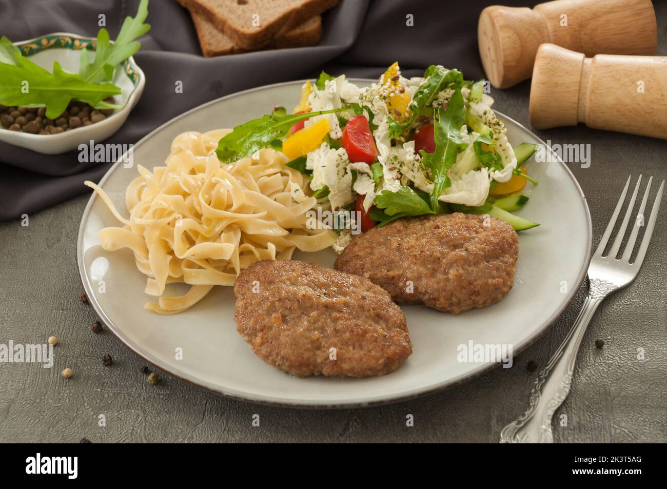 Leckere Koteletts mit Nudeln und Salat auf einem grauen Teller Stockfoto