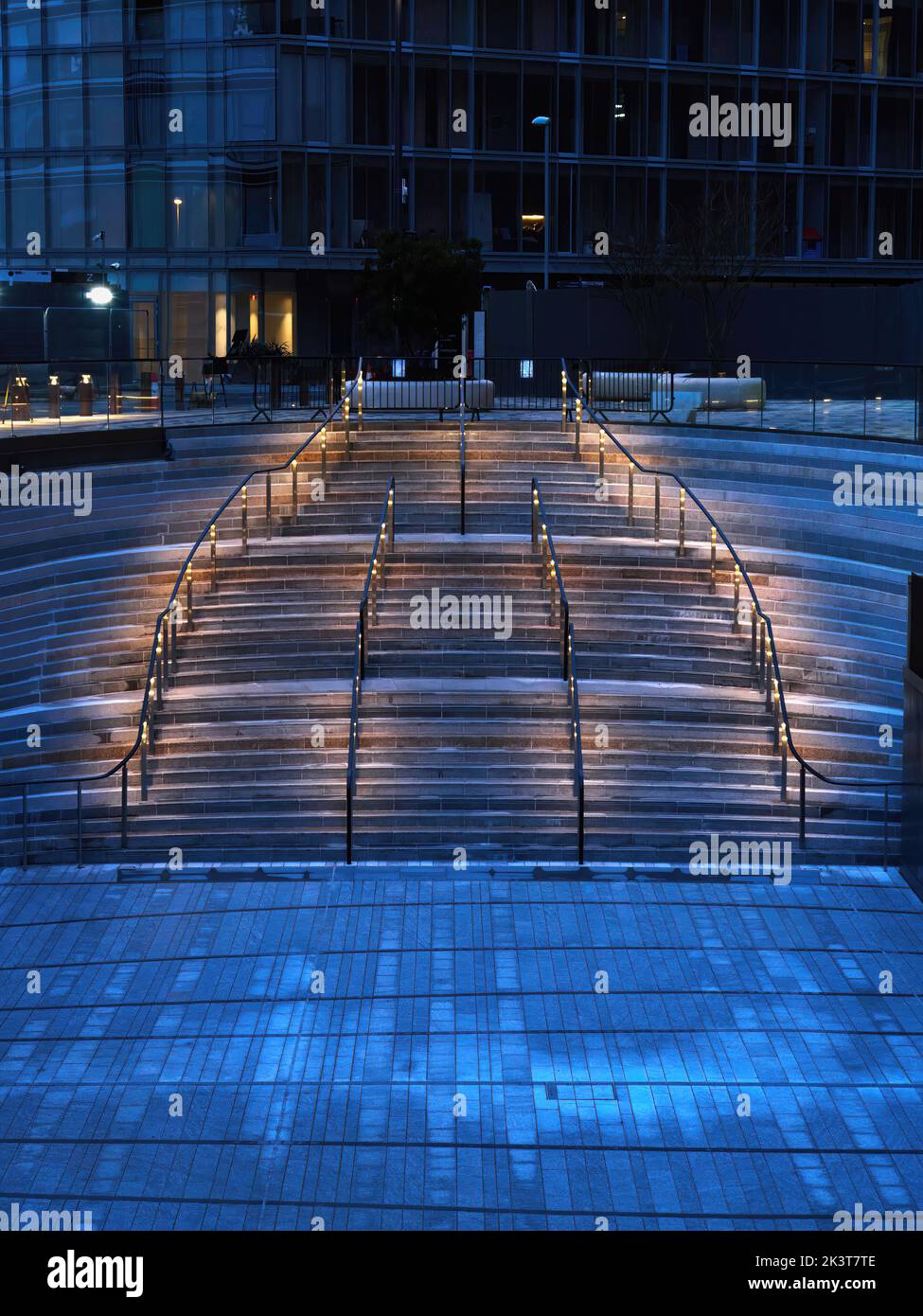Das kühle, blaue Licht des Winterabends wird von einem warmen, glühenden Regenlicht auf einer Amphitheatreppe des neu entwickelten Battersea Power Station durchbrochen. Stockfoto