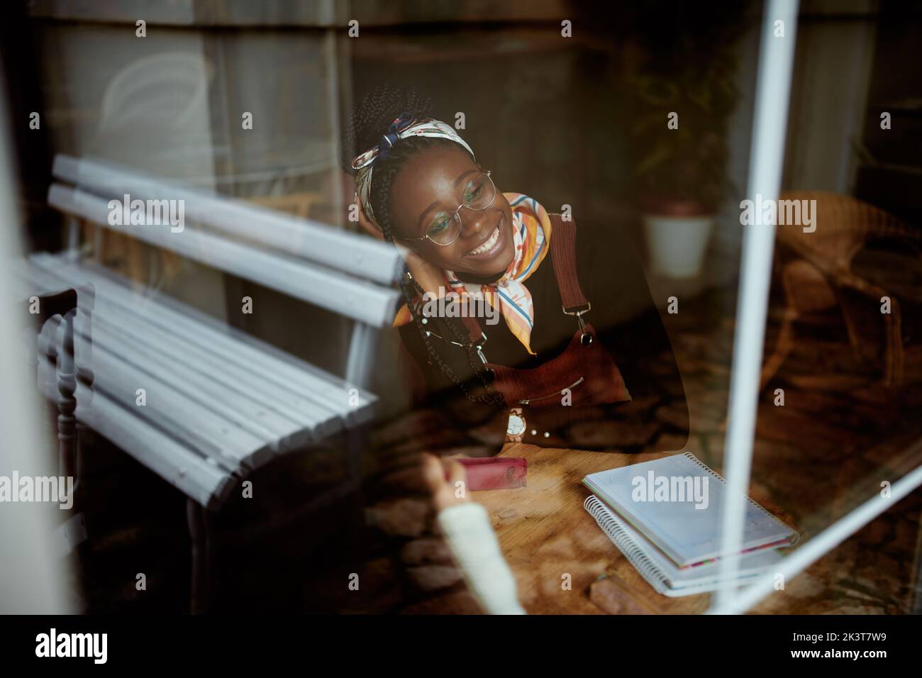 Ein schickes afrikanisches College-Mädchen sitzt in der Cafeteria und studiert für eine Prüfung. Das Bild wurde von außen aufgenommen. Ein Mädchen im Studentenaustausch sitzt Stockfoto