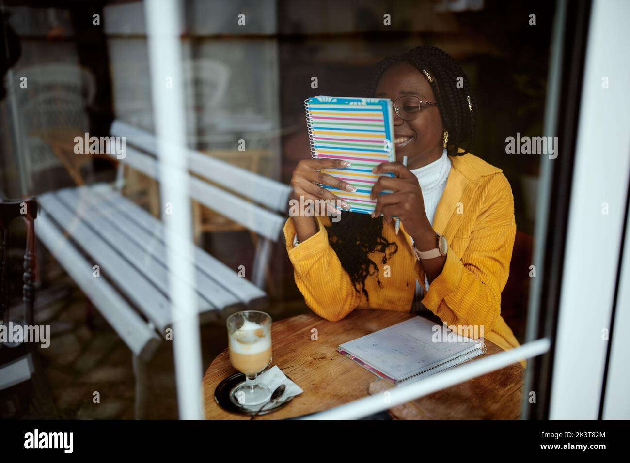 Ein cleveres afrikanisches Mädchen sitzt in einem Café und schaut sich das Lehrbuch an. Stockfoto