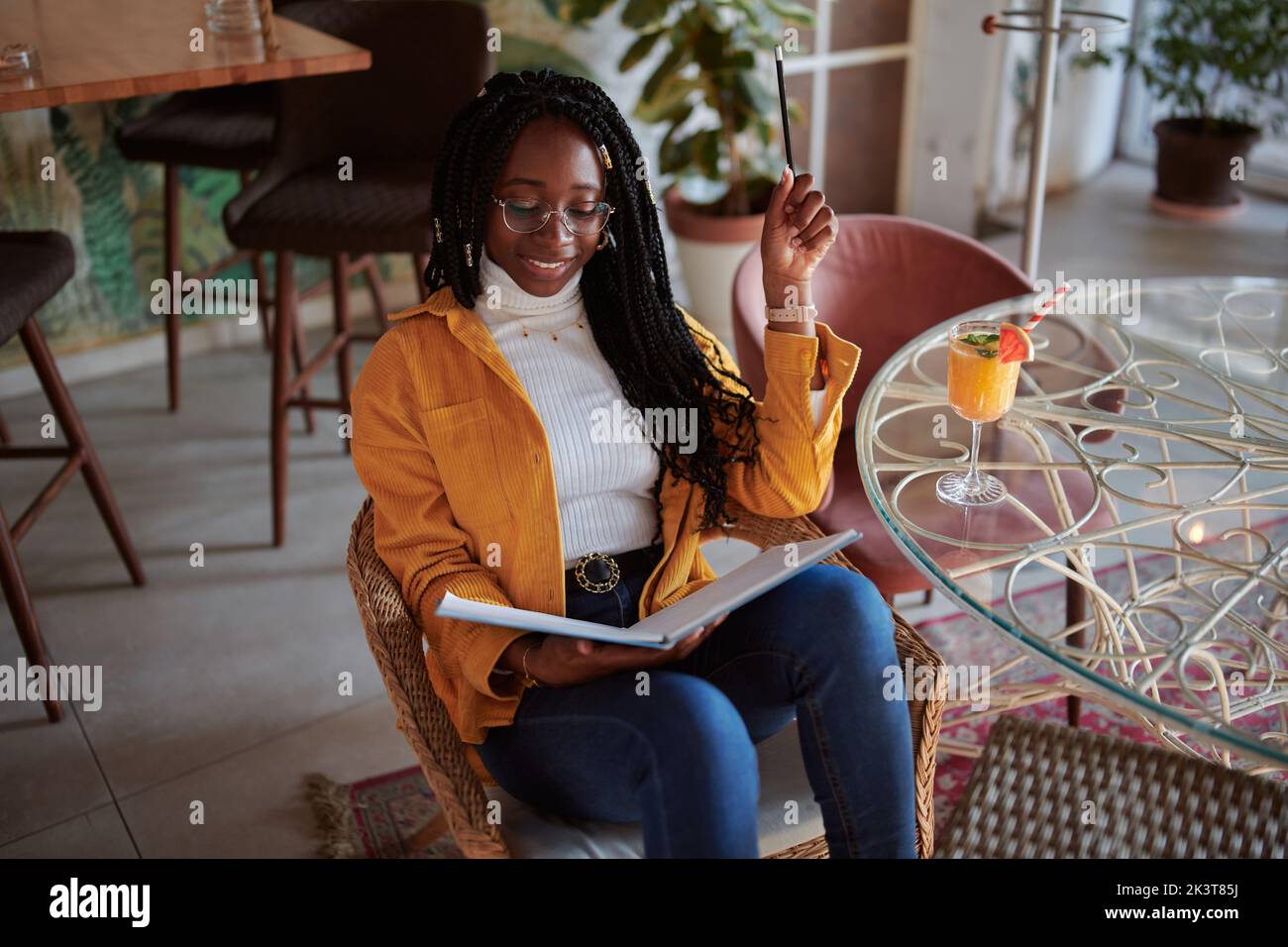 Ein glückliches afrikanisches College-Mädchen sitzt in einem Café mit einem Notizbuch in ihren Händen und studiert für eine Prüfung. Hochschulbildung. Stockfoto
