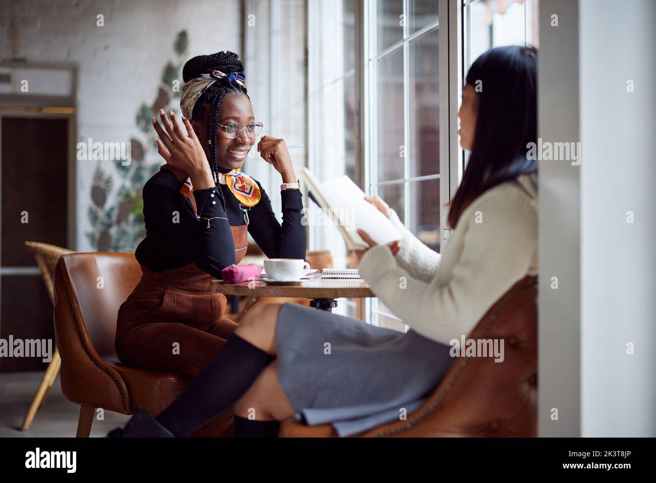 Zwei glückliche multikulturelle Mädchen sitzen in der Cafeteria und studieren für eine Prüfung. Stockfoto