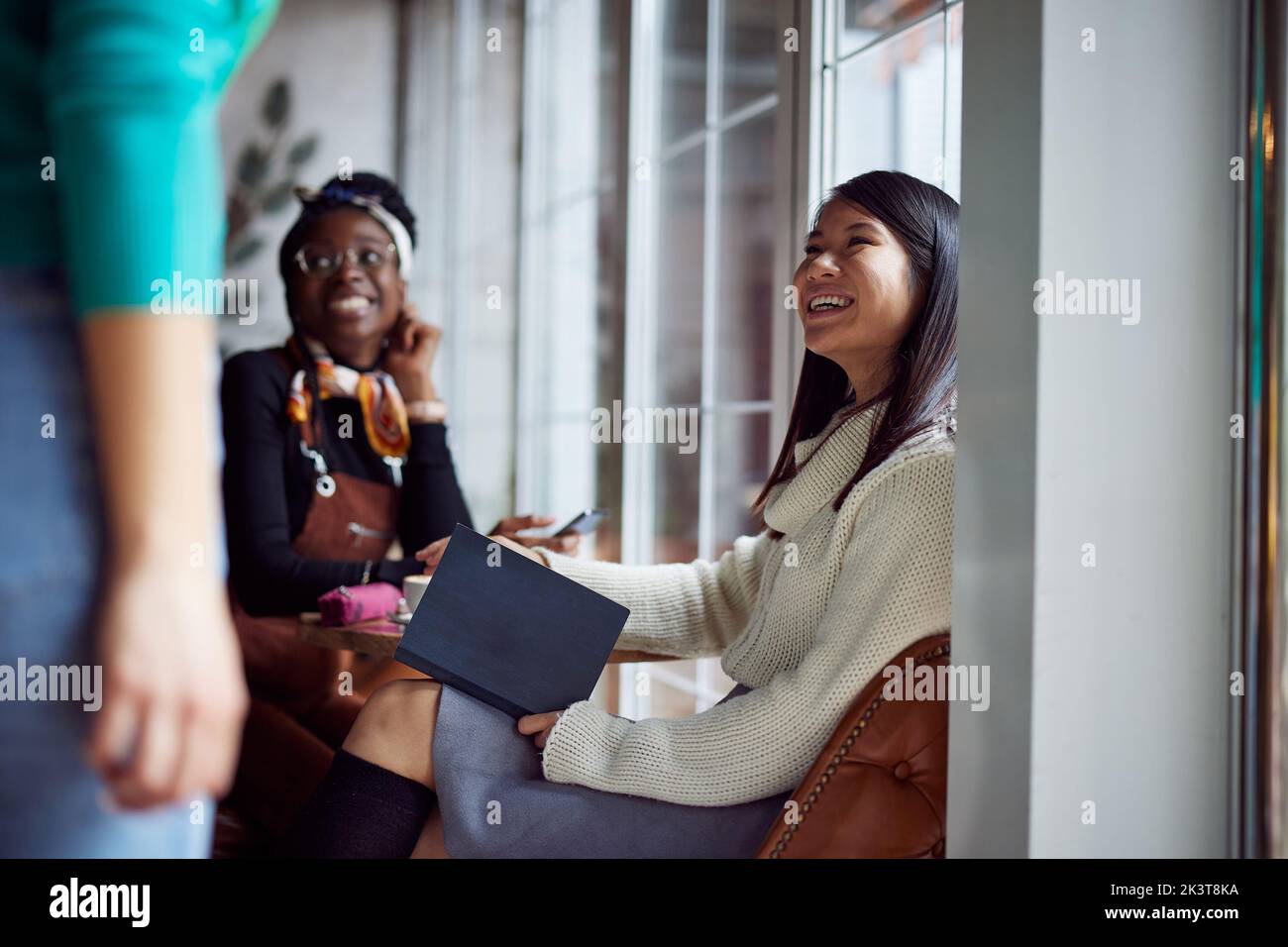 Zwei multikulturelle Mädchen lächeln der Kellnerin beim Lernen im Café zu. Stockfoto