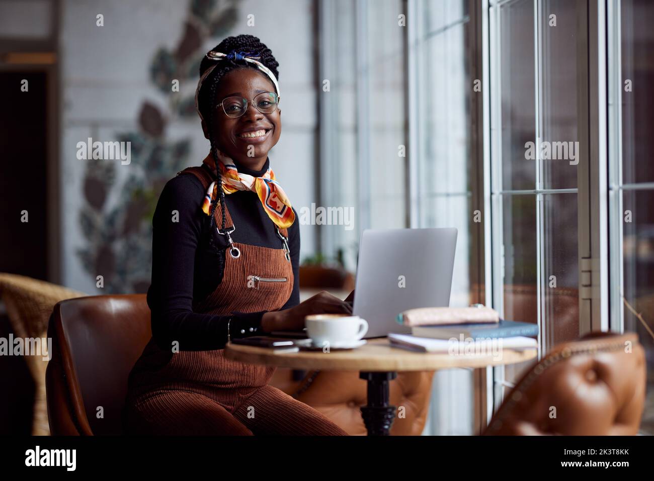 Ein multikulturelles Studentenmädchen sitzt in einem Café und folgt einem Online-Vortrag auf dem Laptop. Stockfoto