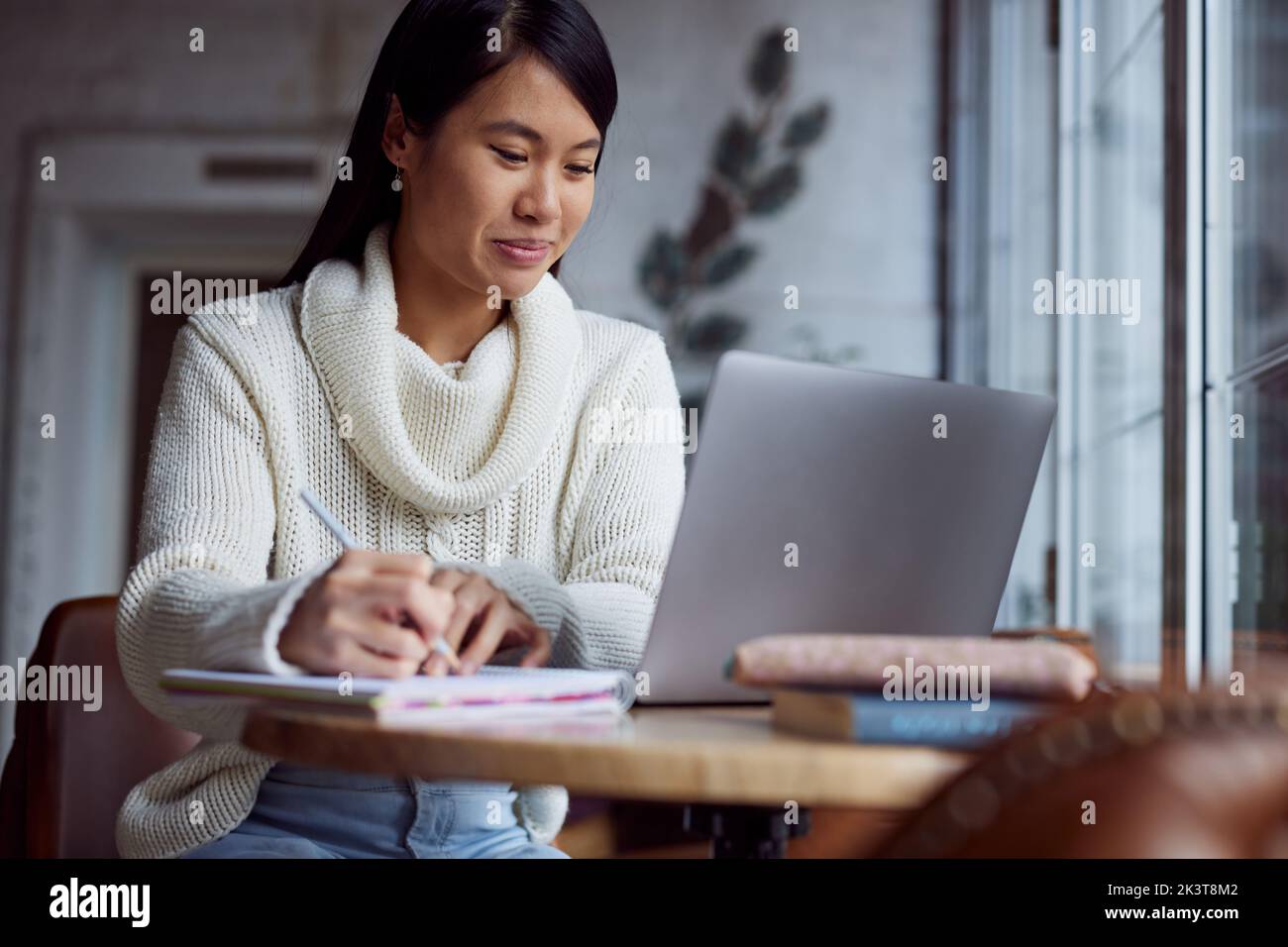 Eine asiatische Studentin sitzt in der Cafeteria und studiert für einen Test. Stockfoto