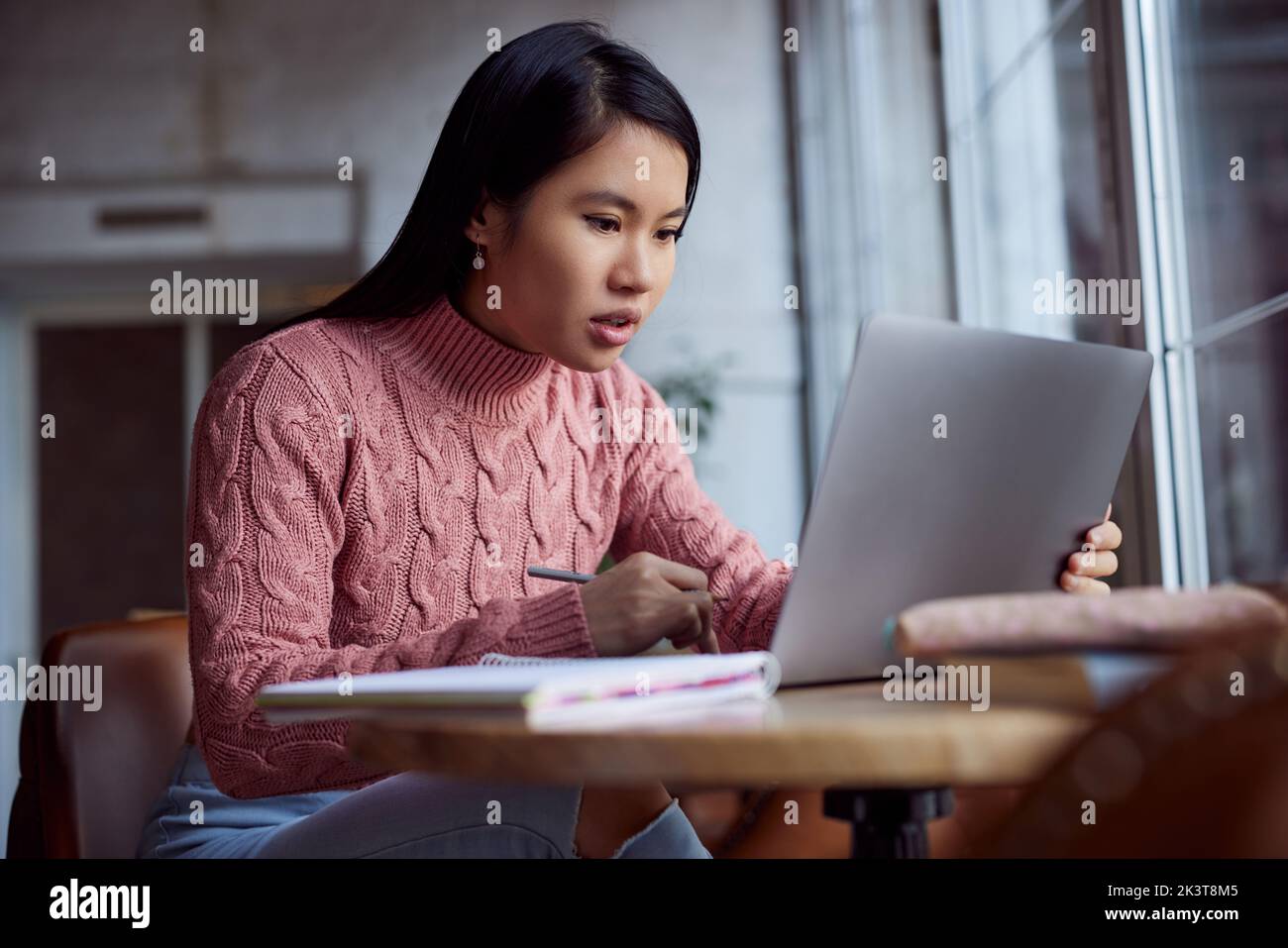 Ein engagiertes multikulturelles College-Mädchen folgt einem Online-Vortrag auf dem Laptop, während es im Café sitzt. Stockfoto