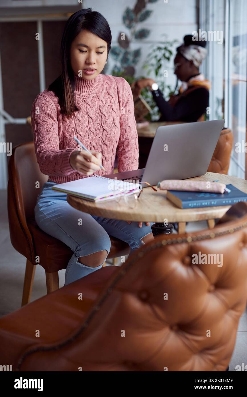 Eine smarte asiatische Studentin sitzt in einem Café und beendet ein Projekt auf ihrem Laptop. Stockfoto