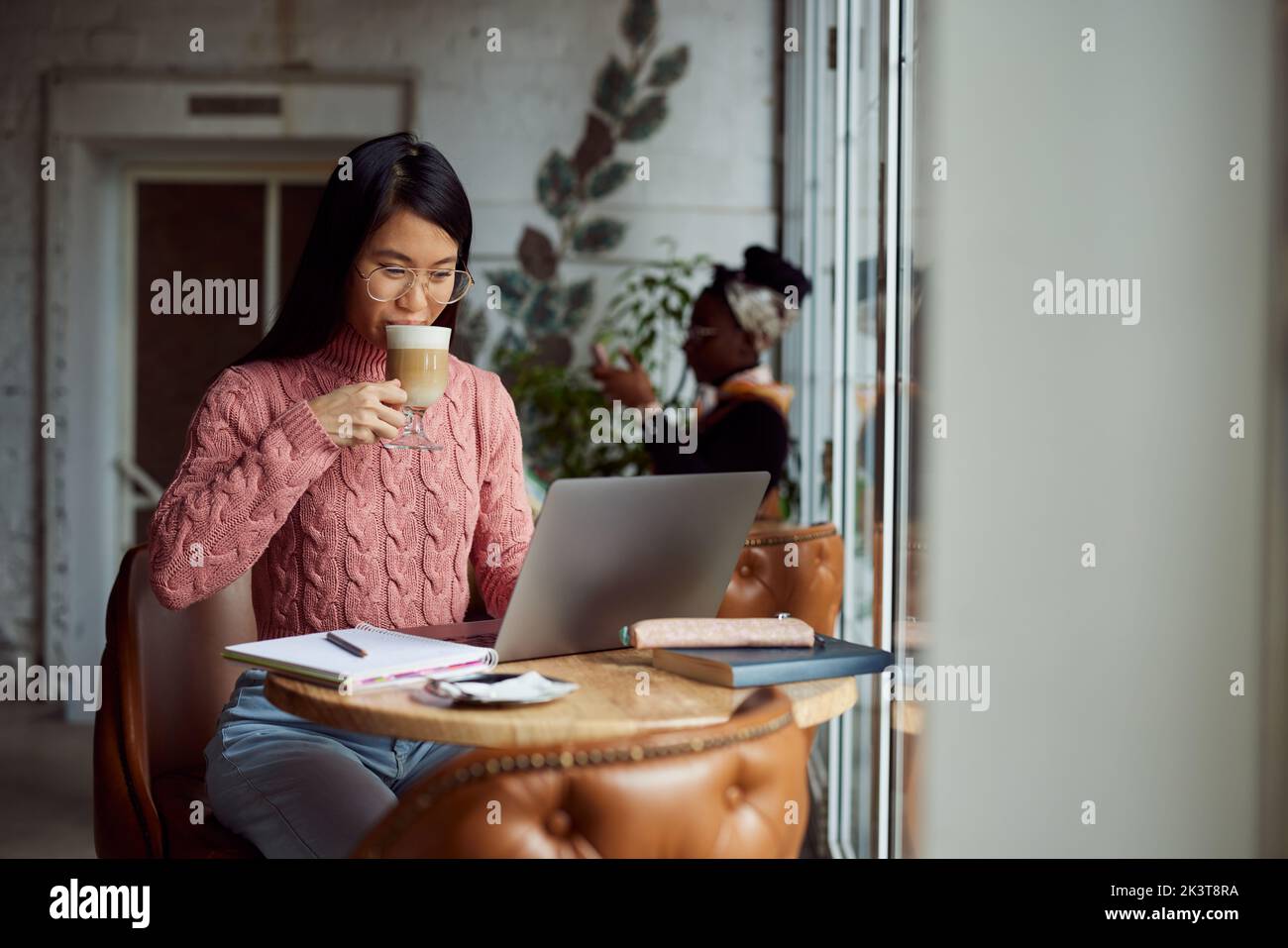 Ein entspannter asiatischer Student sitzt in einem Café, trinkt Kaffee und studiert für einen Test auf dem Laptop. Stockfoto