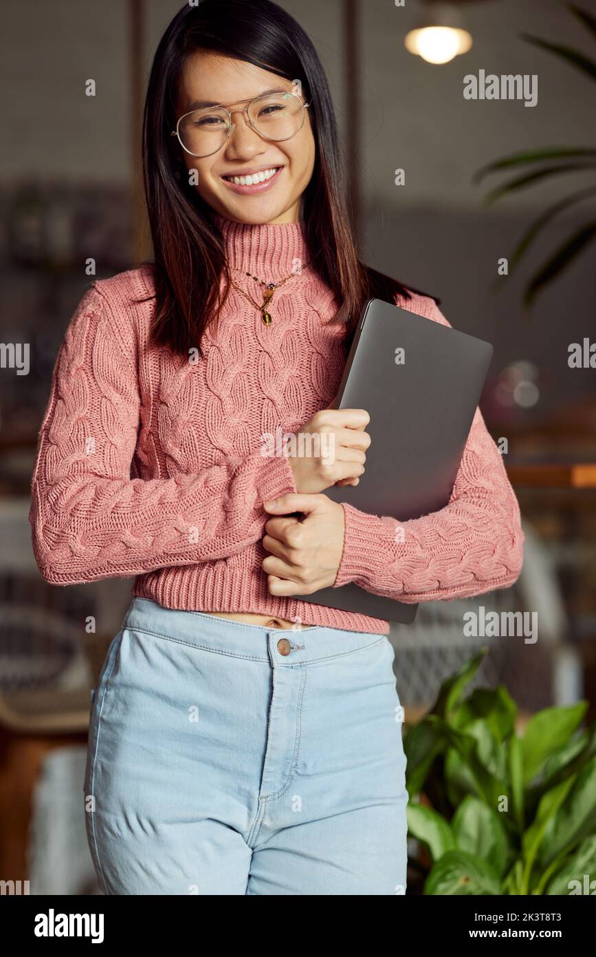 Ein glückliches asiatisches Studentenmädchen hält den Laptop in den Händen und lächelt an der Kamera. Stockfoto