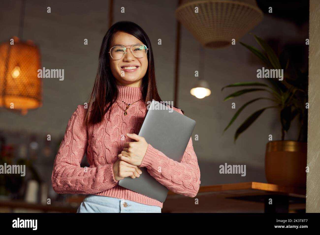 Eine glückliche asiatische Studentin, die in einem Café sitzt und mit einem Laptop in ihren Händen posiert. Stockfoto