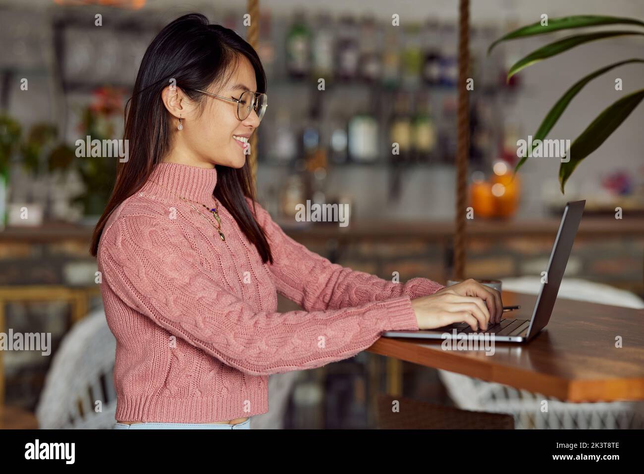 Eine asiatische Studentin macht ihren Auftrag auf einem Laptop, während sie in einem Café sitzt. Stockfoto