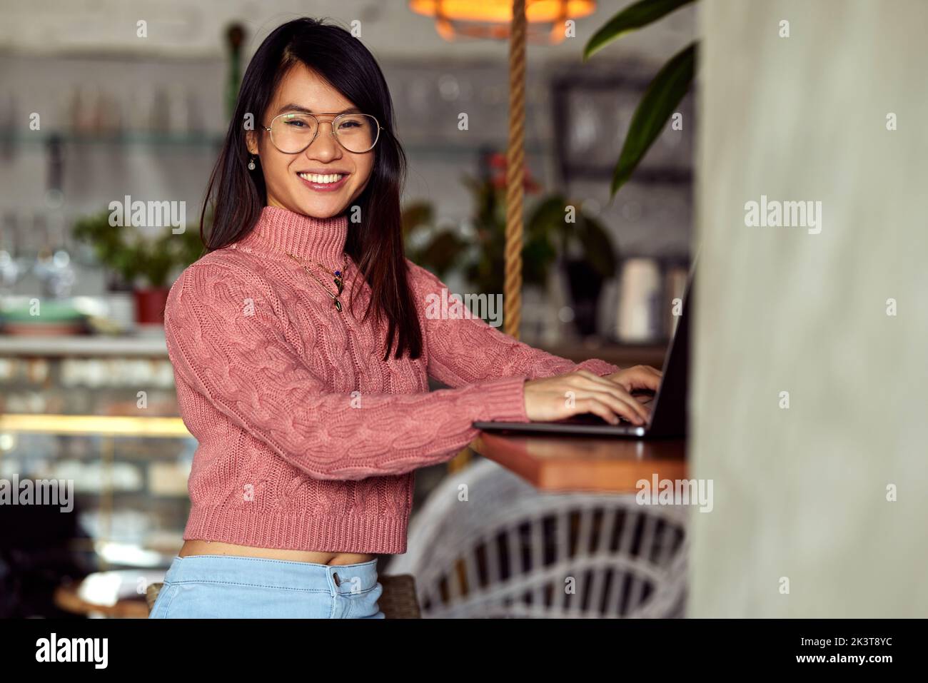Ein glückliches asiatisches Studentenmädchen tippt auf den Laptop und lächelt an der Kamera. Stockfoto