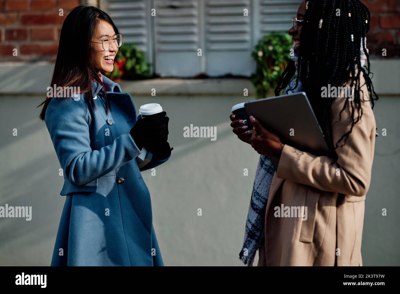 Eine glückliche junge Frau, die ihre Freundin im Café-Garten trifft. Wiedervereinigung, College-Freundschaft. Stockfoto