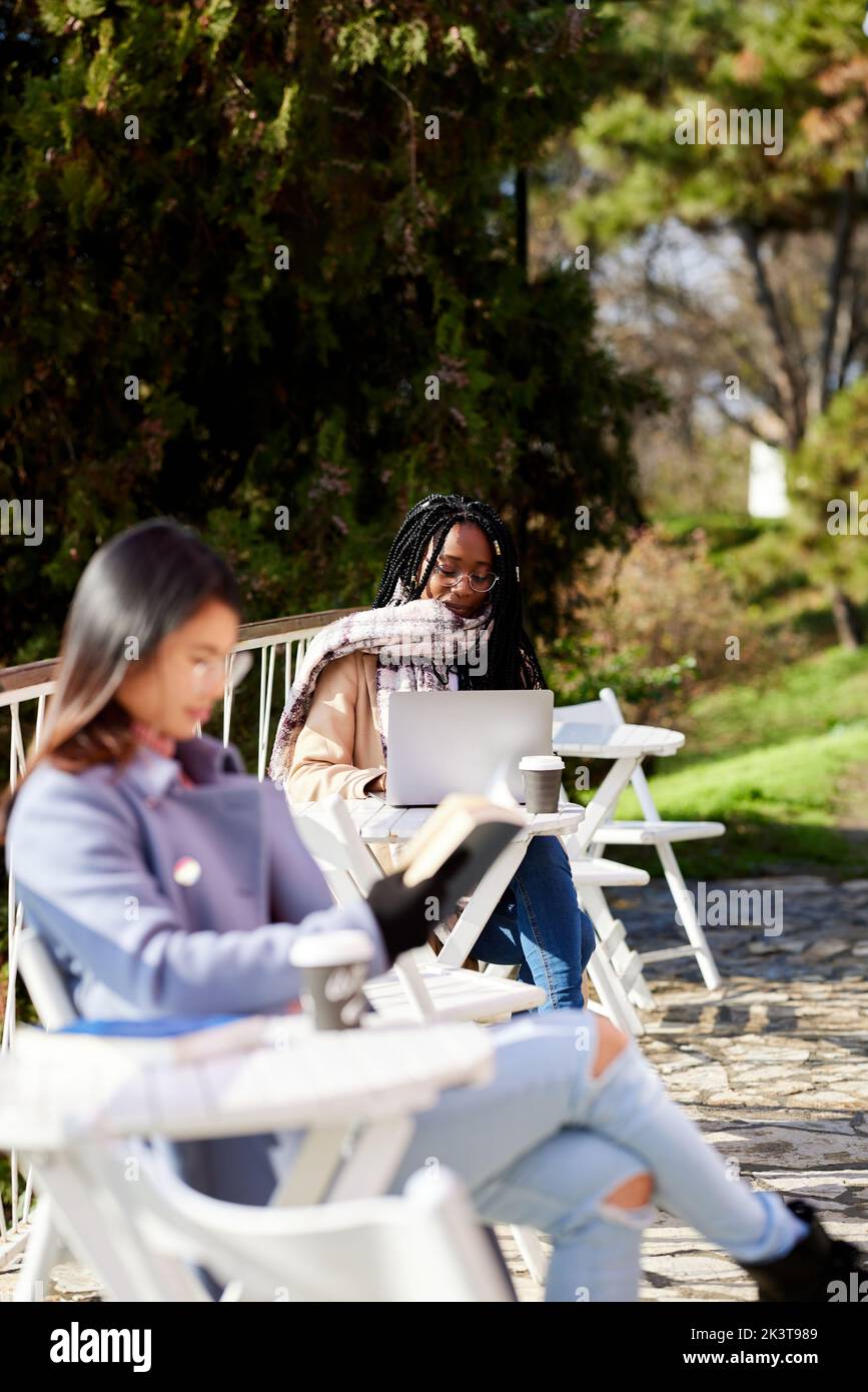 Junge Frauen sitzen in einem Café und verbringen ihre Freizeit mit Arbeit und Lesen. Stockfoto