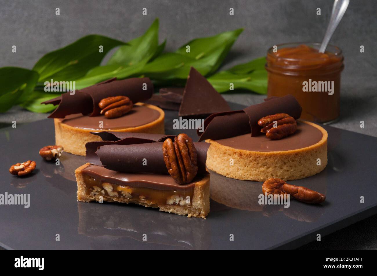 Knuspriges Buttergebäck-Tartlet, gefüllt mit gebratenen Pekannüssen und süßem cremigem Karamell, verziert mit Ganache auf Milchschokolade Stockfoto