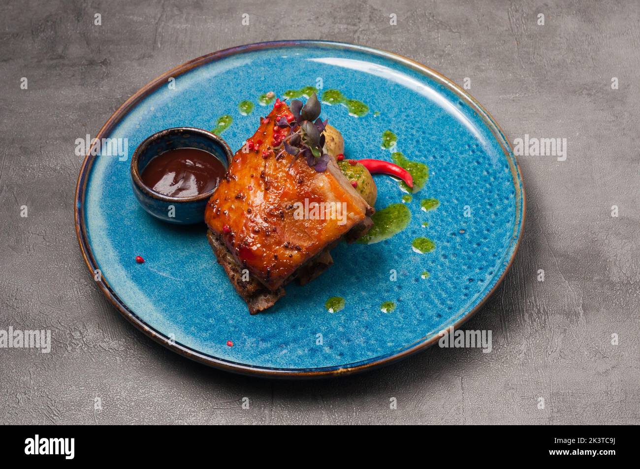 Leckerer Schweinebauch mit neuen Kartoffeln, Tomatensauce und grüner Butter Stockfoto