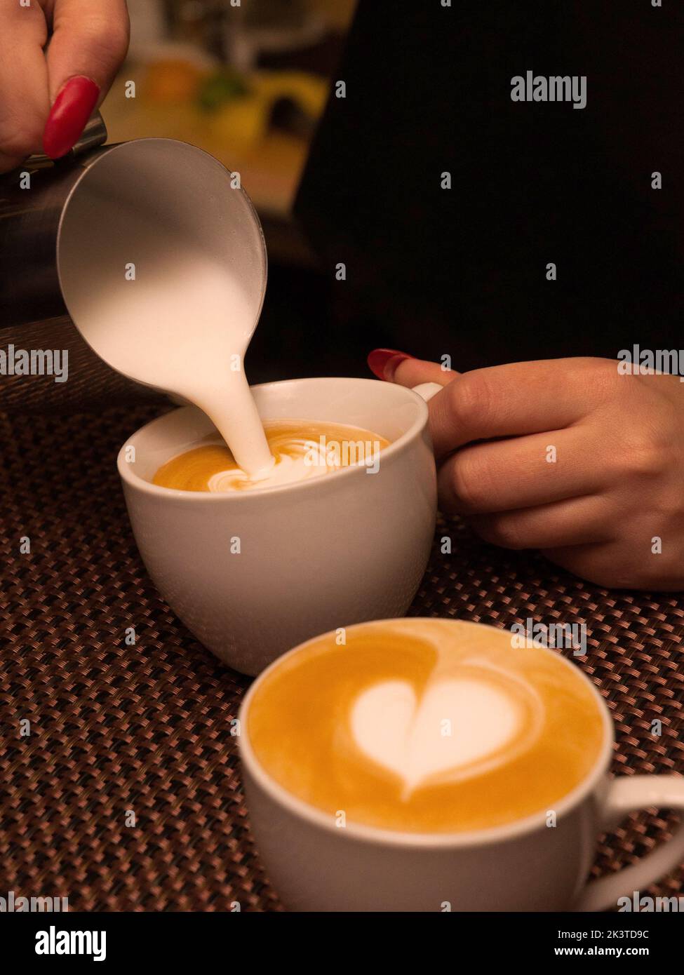 Der Barkeeper gießt Milch in Form eines Herzens in einen Cappuccino Stockfoto