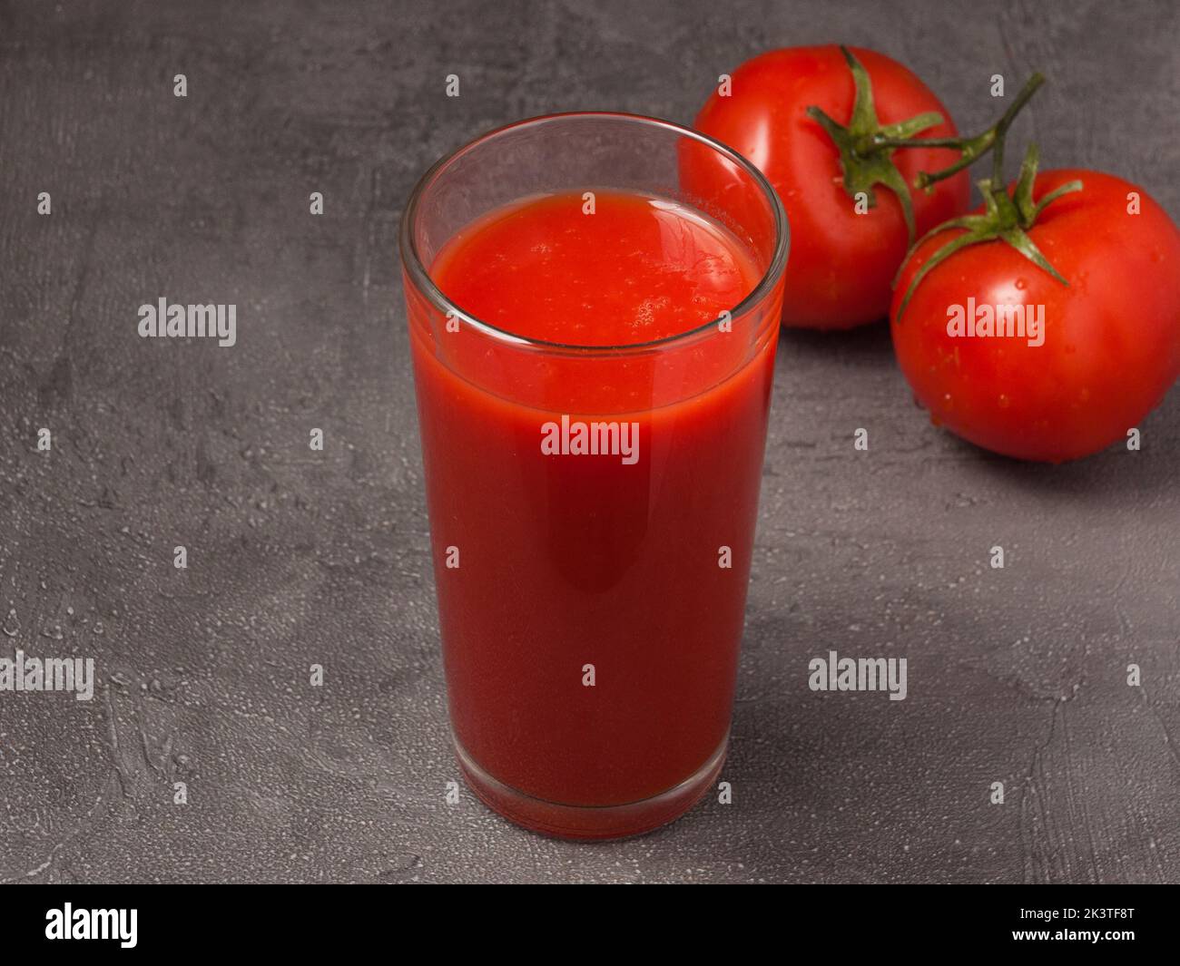 Leckerer Tomatensaft in einem Glas, das mit Tomaten auf grauem Hintergrund dekoriert ist Stockfoto
