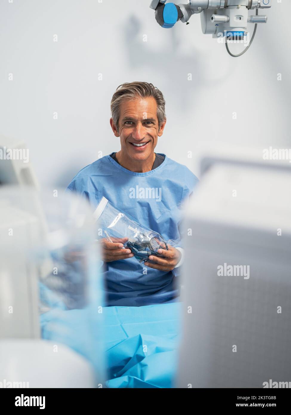 Reifer Mann in medizinischer Uniform lächelt und schaut in die Kamera, während er in einer modernen Klinik arbeitet Stockfoto