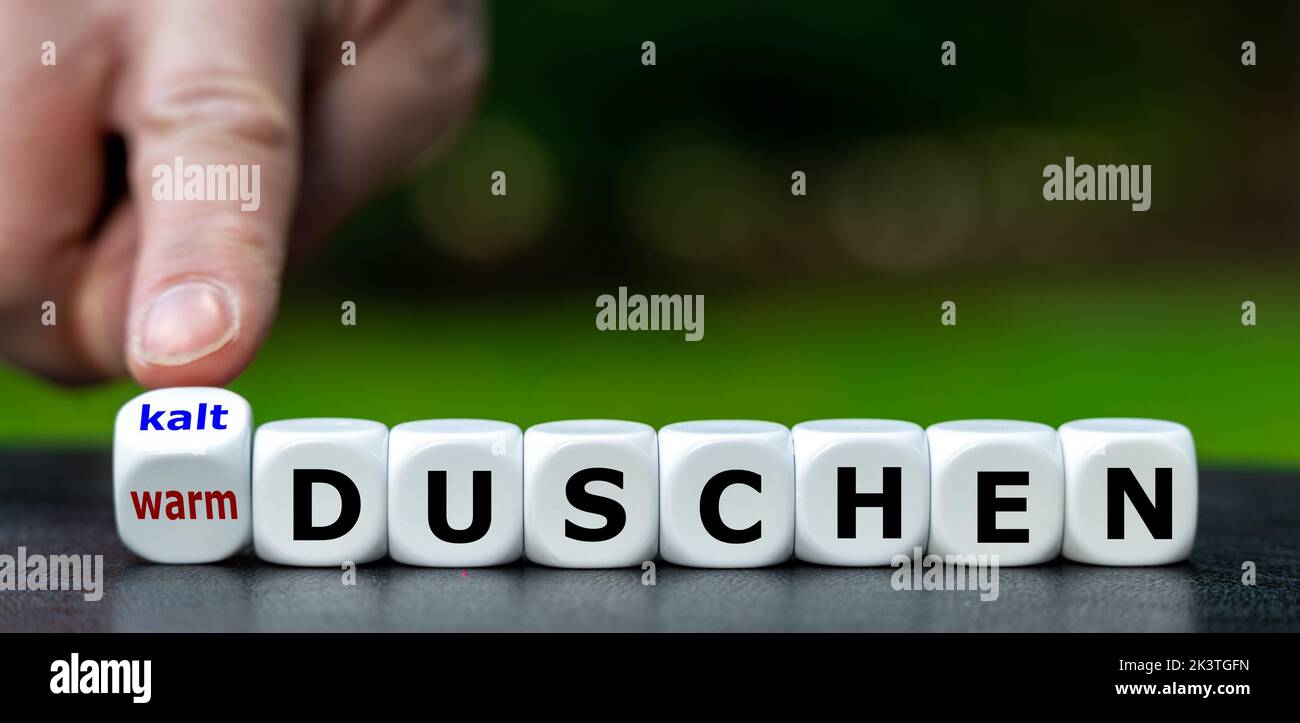Die Hand dreht Würfel und ändert den deutschen Ausdruck 'warm duschen' in 'kalt duschen'. Stockfoto