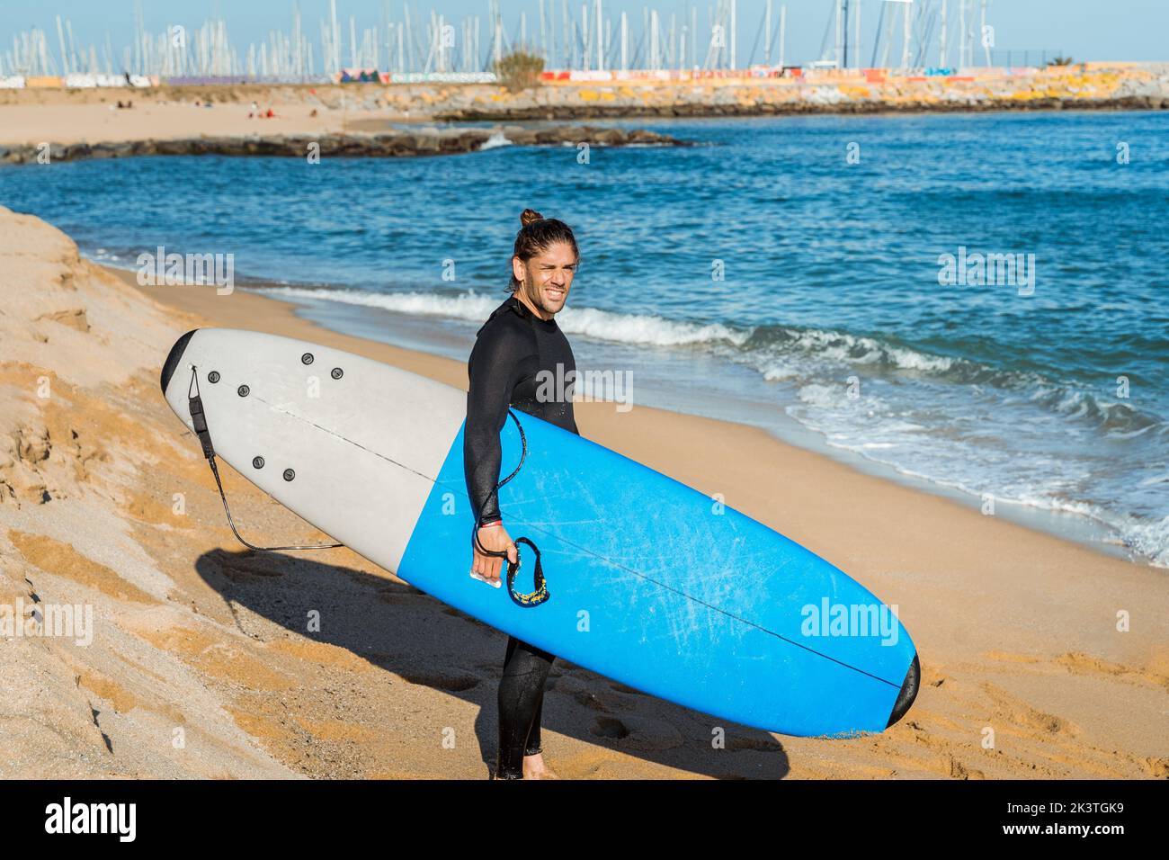 Seitenansicht eines jungen, nachdenklichen Mannes mit Surfbrett in den Händen, der am Sandstrand in der Nähe des winkenden Meeres steht und wegschaut, während er sich auf das gemeinsame Surfen vorbereitet Stockfoto