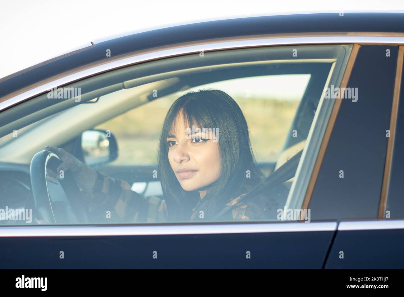 Durch das Fenster einer jungen lateinamerikanischen Frau mit langen dunklen Haaren, die auf dem Land Auto fährt und wegschaut Stockfoto