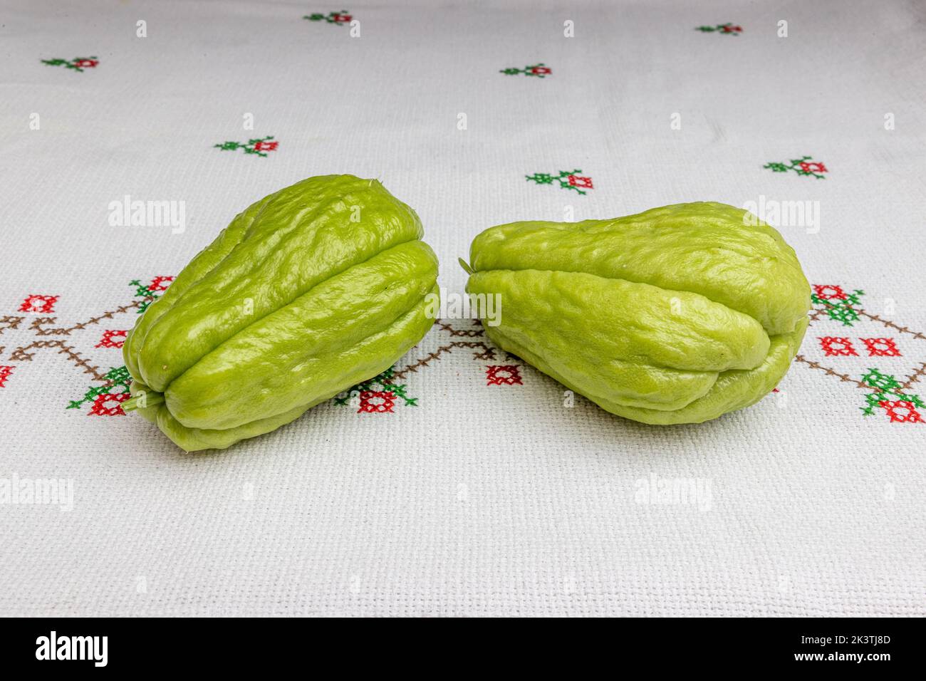 Zwei biologisch angebaute Chayote auf einer Tischdecke mit roten Blüten in Kreuzstich, auch bekannt als: labu siam, jipang. Konzept von Bio, Bio und Natur Stockfoto