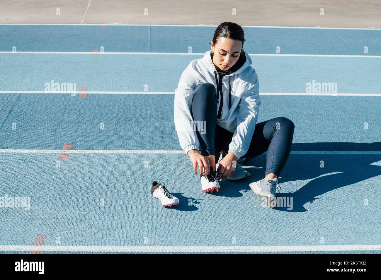 Sportlerin in Sportbekleidung sitzt auf der Rennstrecke und wechselt die Schuhe während des Trainings auf der Rennstrecke an einem sonnigen Tag im Stadion Stockfoto