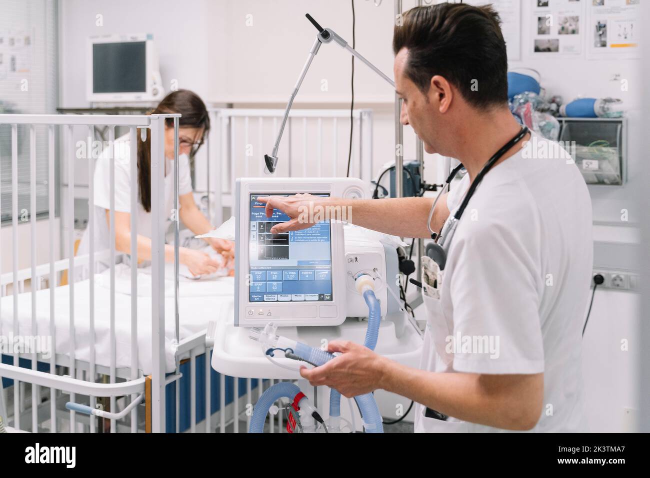 Seitenansicht des Arztes männliche Einstellparameter medizinisches Gerät für die künstliche Atmung in der Station mit Krankenschwester untersucht Baby auf dem Hintergrund Stockfoto