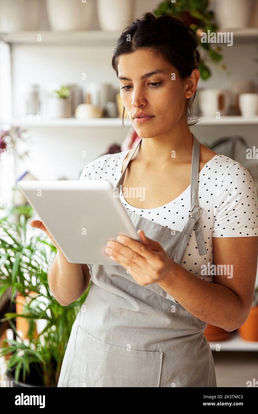 Junge Erwachsene weibliche Baumschulbesitzer Scrollen auf digitalen Tablet Stockfoto