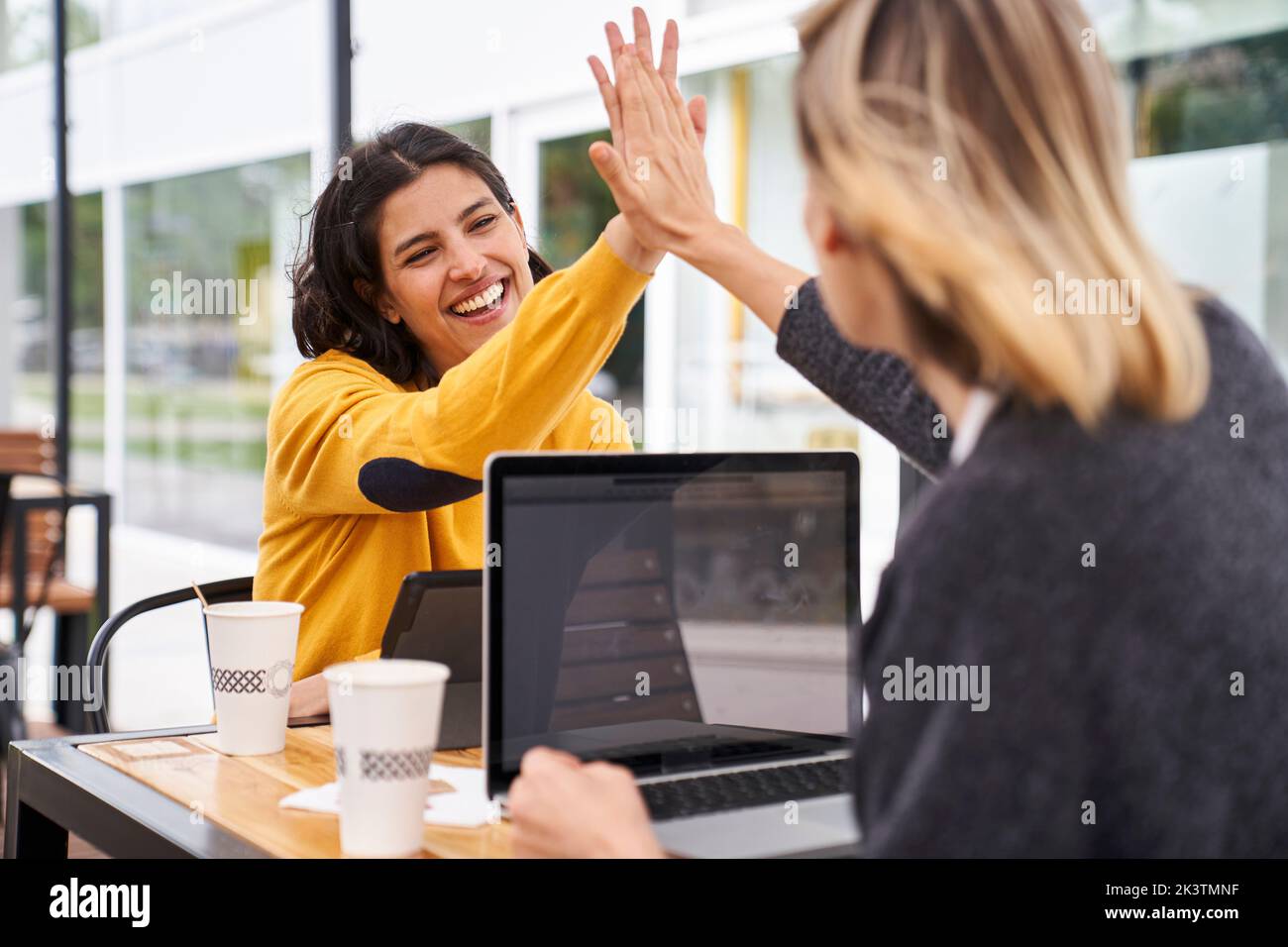 Aufnahme von zwei weiblichen Arbeitskollegen, die sich beim Arbeiten im Freien gegenseitig hoch fiving Stockfoto