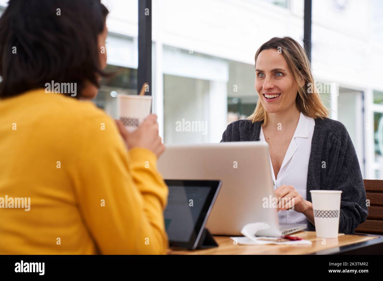 Mittellange Aufnahme von zwei weiblichen Mitarbeitern, die im Außenbüro über Geschäftsthemen sprechen Stockfoto