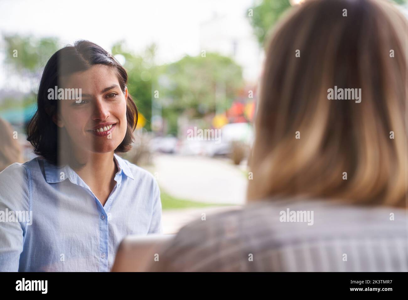 Mitten in der Aufnahme einer lateinamerikanischen Mitarbeiterin, die im Außenbüro mit ihrer Kollegin über Arbeitsfragen sprach Stockfoto