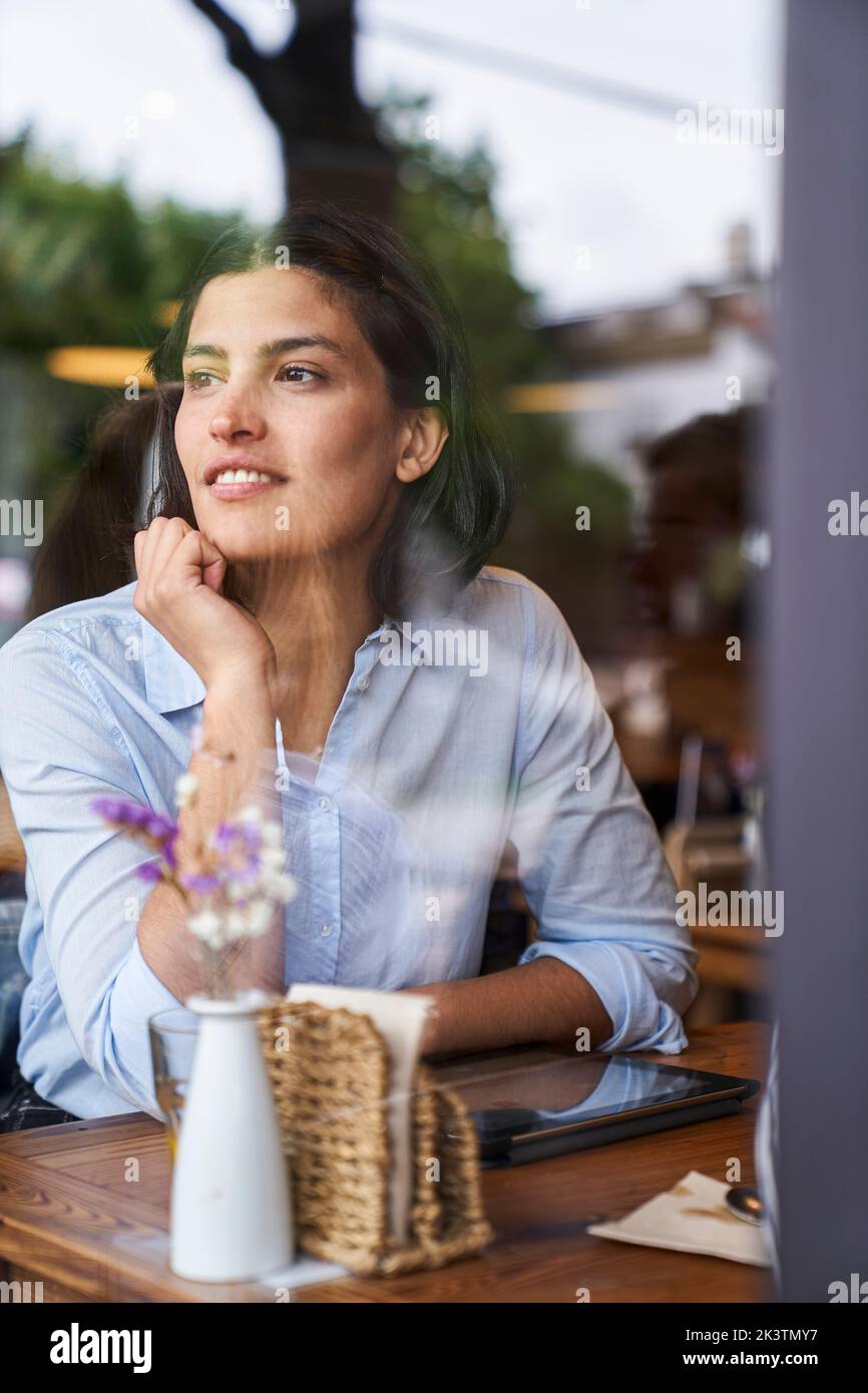 Foto, das durch das Fenster geschossen wurde, auf dem eine lateinamerikanische Frau in Gedanken im Café sitzt Stockfoto