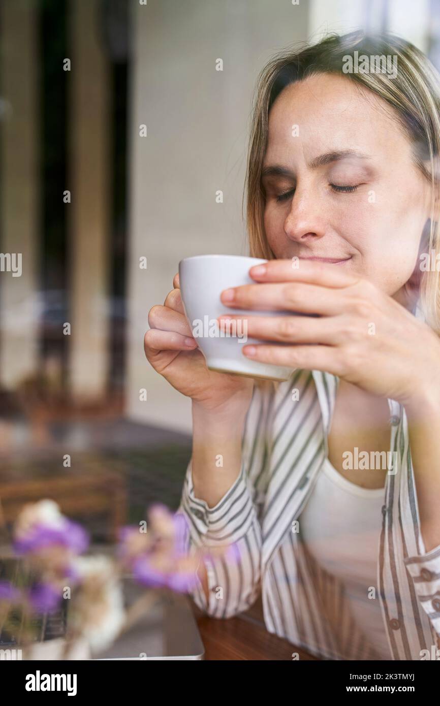 Porträt einer attraktiven Frau, die mit geschlossenen Augen eine Tasse Kaffee in den Händen hält Stockfoto