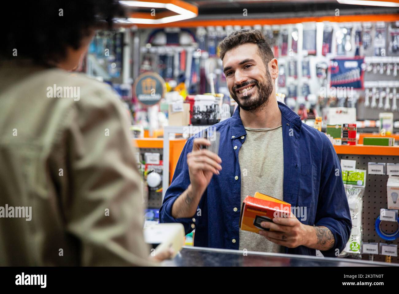 Ein männlicher Kunde zahlt mit Kreditkarte an einen afroamerikanischen Arbeiter im Eisenwarengeschäft Stockfoto