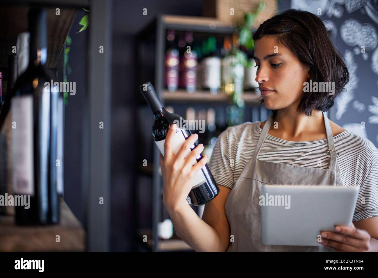 Eine Arbeiterin im Weingeschäft liest das Etikett der Weinflasche Stockfoto