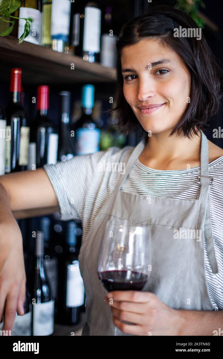 Sommelierin hält ein Glas Wein in der Hand, während sie im Spirituosenladen steht Stockfoto