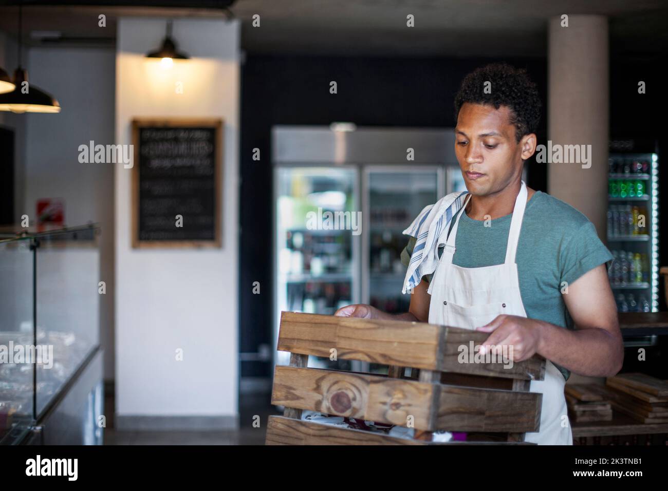 Nachdenklicher junger lateinamerikanischer Lebensmittelhändler mit Holzkiste Stockfoto