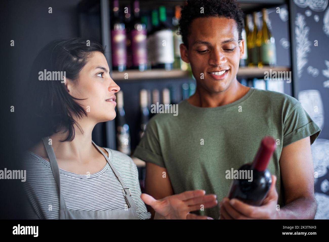 Angestellte im Spirituosengeschäft, die mit dem Kunden über eine Weinflasche sprach Stockfoto