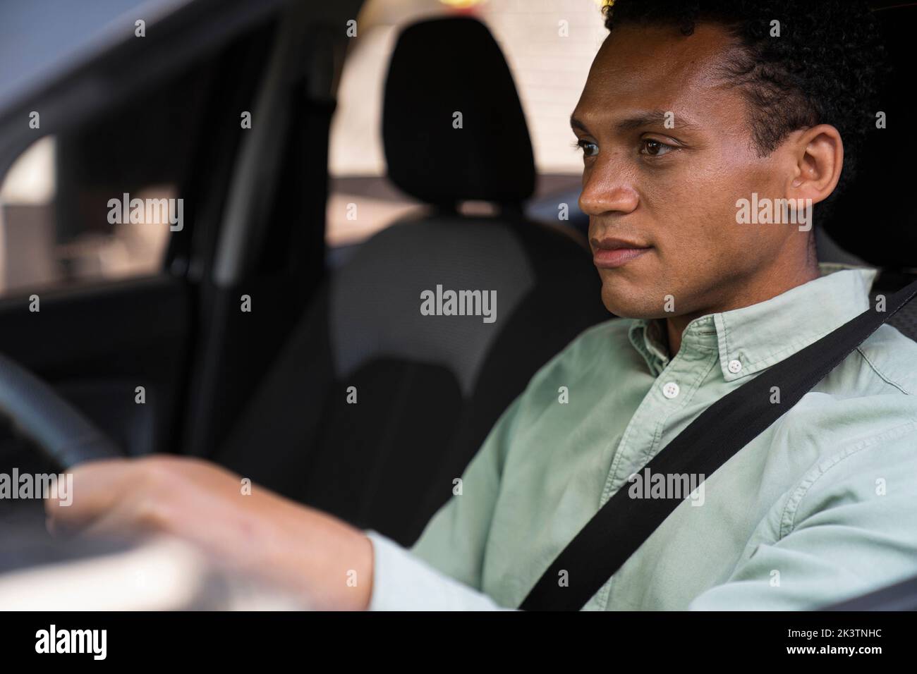 Mid-Shot-Porträt, das von außerhalb des Fahrzeugs des afroamerikanischen Geschäftsmannes aufgenommen wurde, der sein Auto zur Arbeit fährt Stockfoto