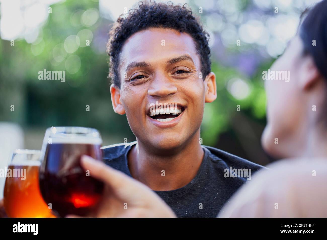Lateinamerikanischer junger Mann, der die Kamera anschaut, während er mit Freunden Bier trinkt Stockfoto