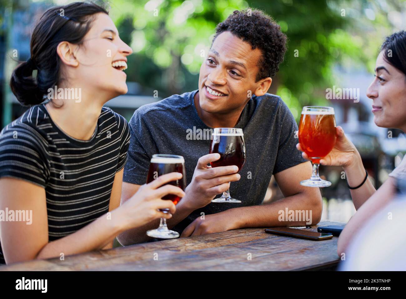 Junger lateinamerikanischer Mann, der mit Freundinnen Bier trinkt Stockfoto