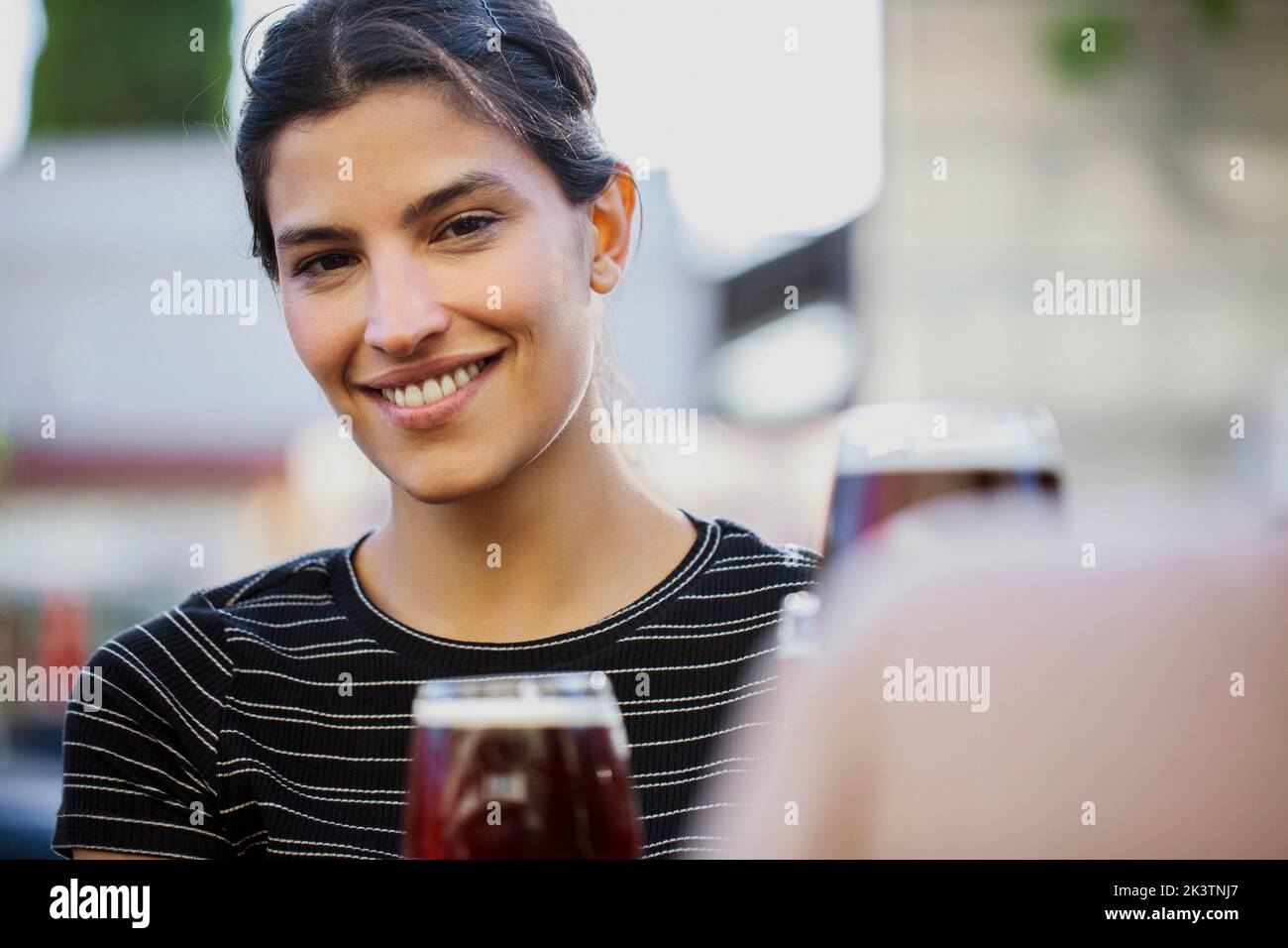 Junge Frau lächelt und schaut auf die Kamera, während sie an der Bar im Freien sitzt Stockfoto