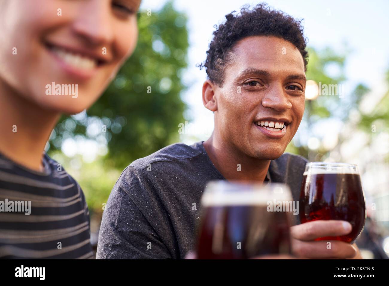 Porträt eines glücklichen jungen afroamerikanischen Mannes, der vor der Kamera lächelt und dabei ein Glas Bier in der Hand hält Stockfoto