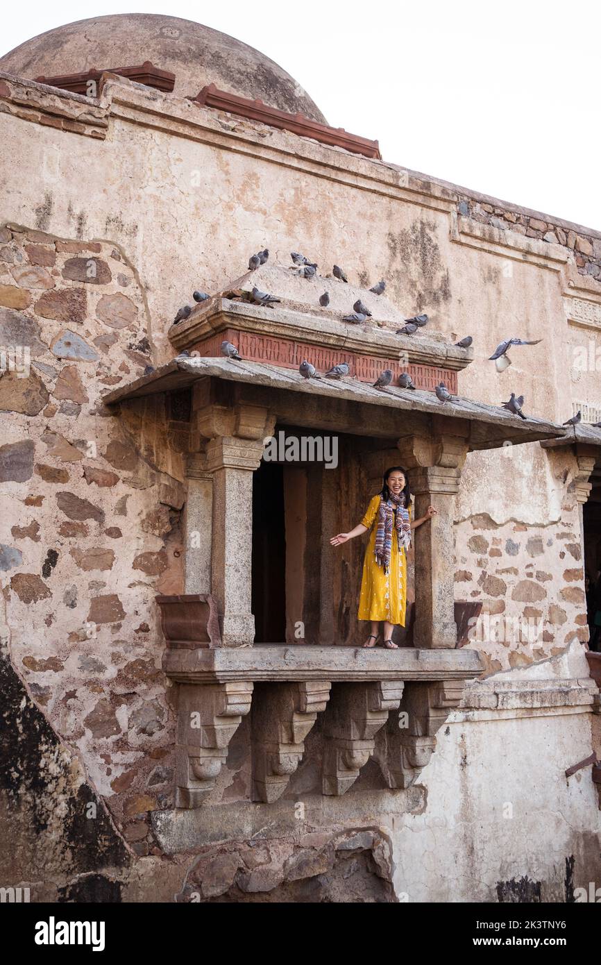 Glückliche ethnische asiatische Frau, die auf einem alten Balkon unter dem Dach mit einer Taubenschar steht, während sie das Dorf Hauz Khas in Neu-Delhi Indien besucht Stockfoto